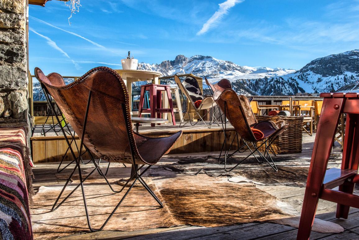 Fauteuils et tabourets sur la terrasse du Grrizzly Bar à Courchevel avec vue sur la montagne