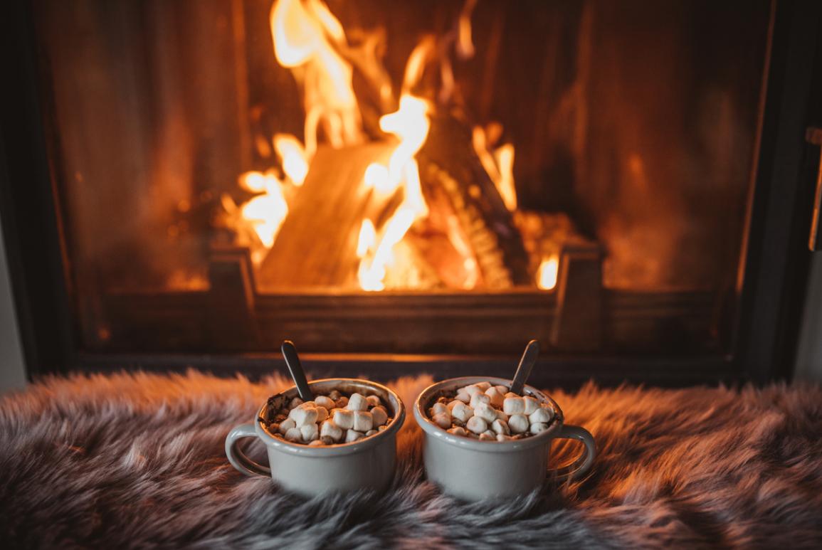 Deux chocolats chauds avec de la guimauve posés sur une couverture auprès d'un feu de cheminée à l'hôtel Courcheneige