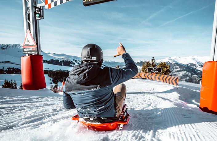 Un homme de dos qui descend la piste sur une luge à Courchevel