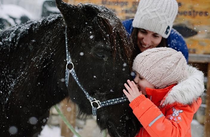 Une enfant qui embrasse un cheval dans la neige